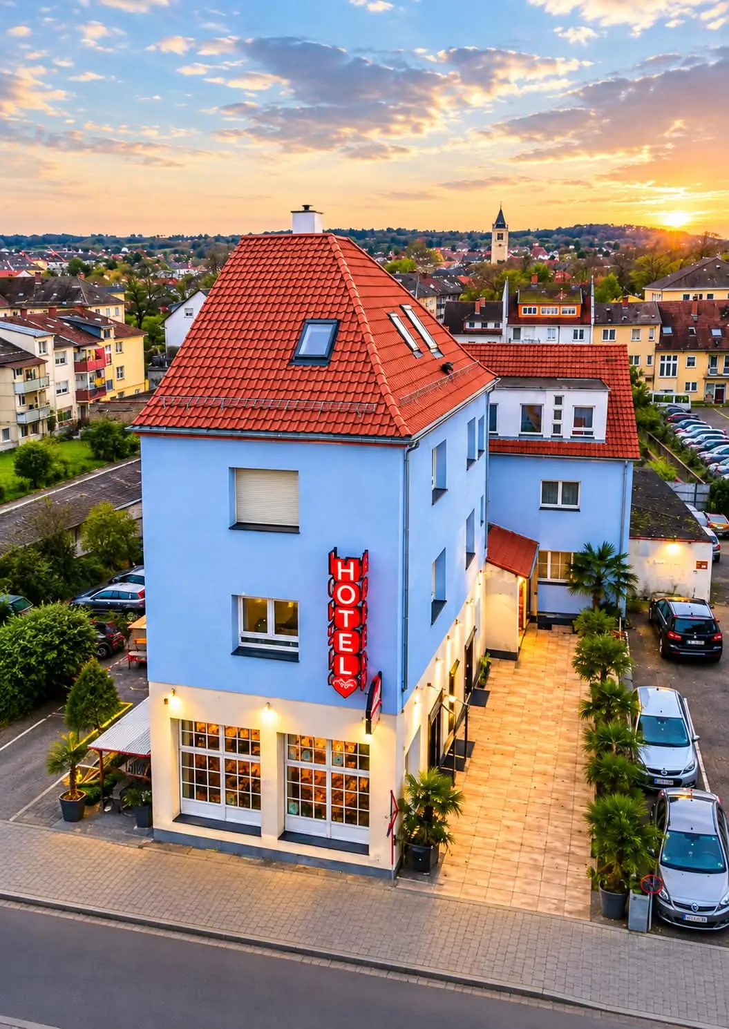 Das hellblaue Hotel Bruchsal Herz mit rotem Ziegeldach und leuchtendem HOTEL-Schild in der Abendsonne